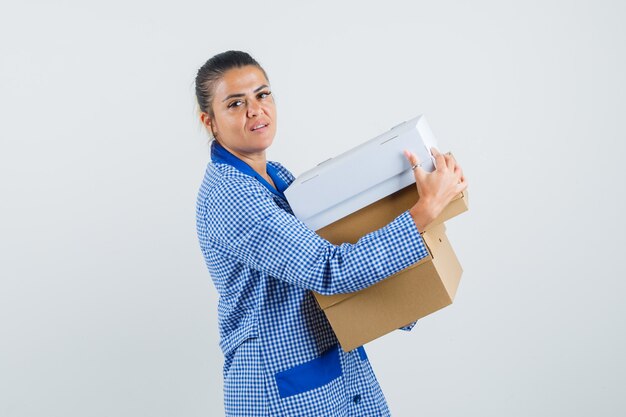 Young woman in blue gingham pajama shirt holding boxes and looking pretty , front view.