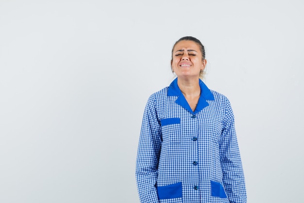 Young woman in blue gingham pajama shirt standing straight and posing and looking harried , front view.