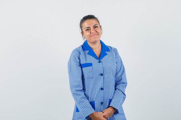 Young woman in blue gingham pajama shirt standing straight and posing and looking pretty , front view.