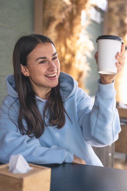 青いパーカーを着た若い女性がカフェで朝のコーヒーを楽しんでいます