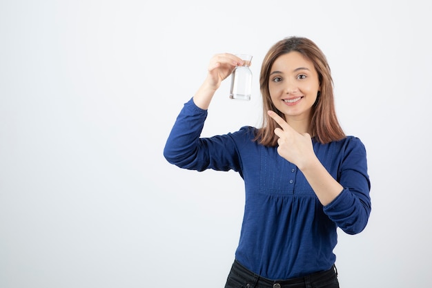 白い壁の上の彼女の手で水を指している青い服を着た若い女性。