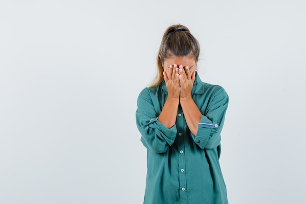 Young woman in blue shirt holding hands on her face and looking upset