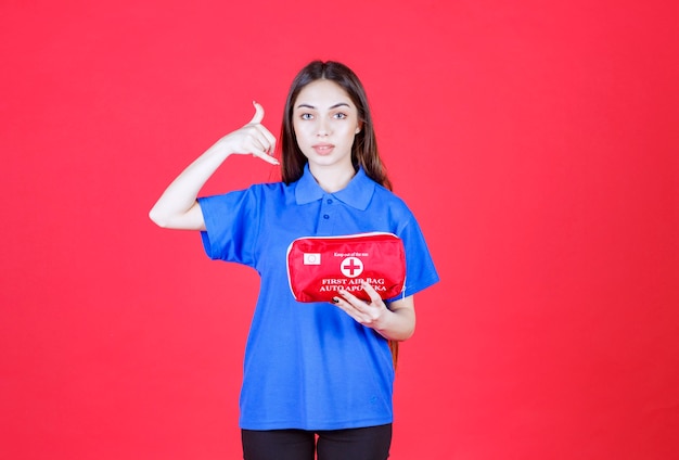 Young woman in blue shirt holding a red first aid kit and asking for a call