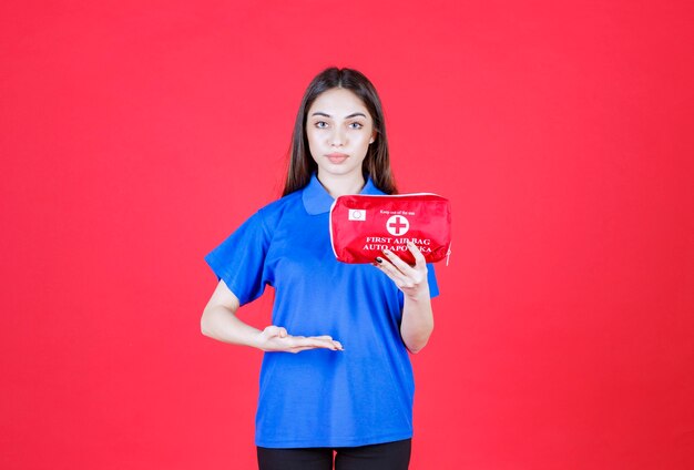 Young woman in blue shirt holding a red first aid kit