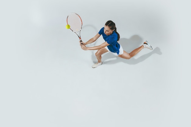 테니스 블루 셔츠에 젊은 여자. 그녀는 라켓으로 공을칩니다. 흰색 절연 실내 샷입니다. 젊음, 유연성, 힘 및 에너지. 부정적인 공간. 평면도.