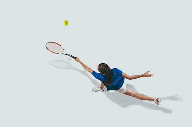Young woman in blue shirt playing tennis. She hits the ball with a racket.