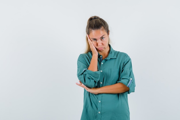 Young woman in blue shirt pushing her cheek up and looking unexciting