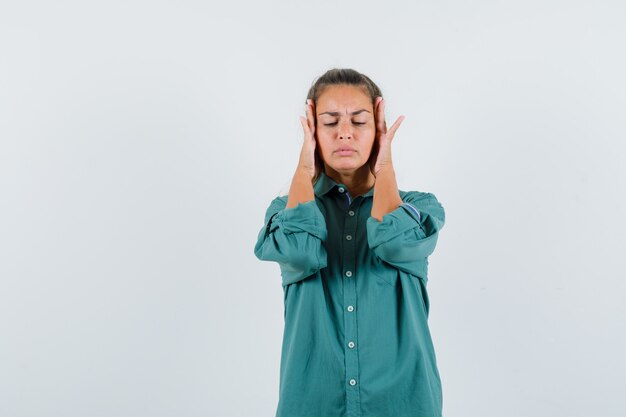 Young woman in blue shirt rubbing her temple and looking painful