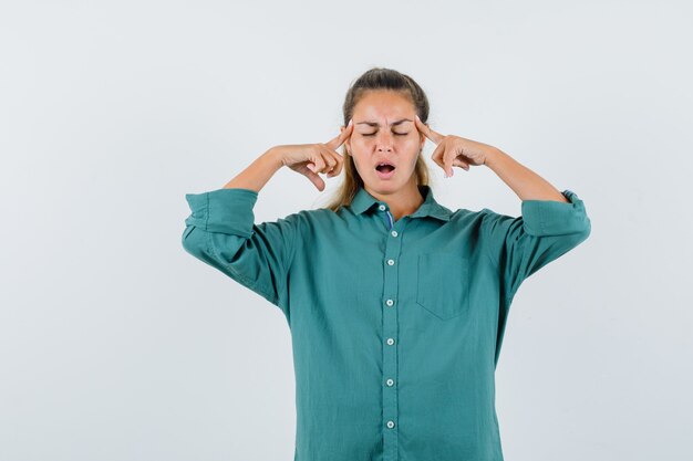 Young woman in blue shirt rubbing her temple and looking troubled