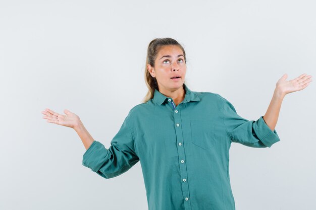 Giovane donna in camicia blu che mostra gesto impotente e che sembra confusa