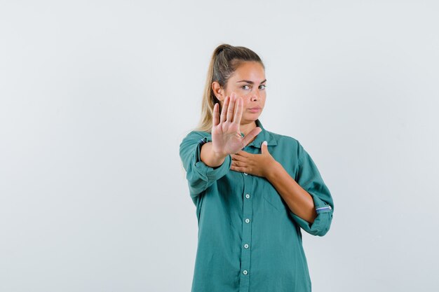 Молодая женщина в синей рубашке показывает жест отказа и выглядит серьезной