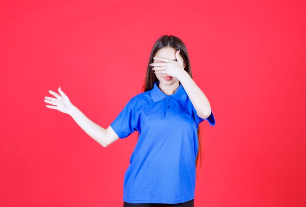 Young woman in blue shirt standing on red wall and pointing at someone around