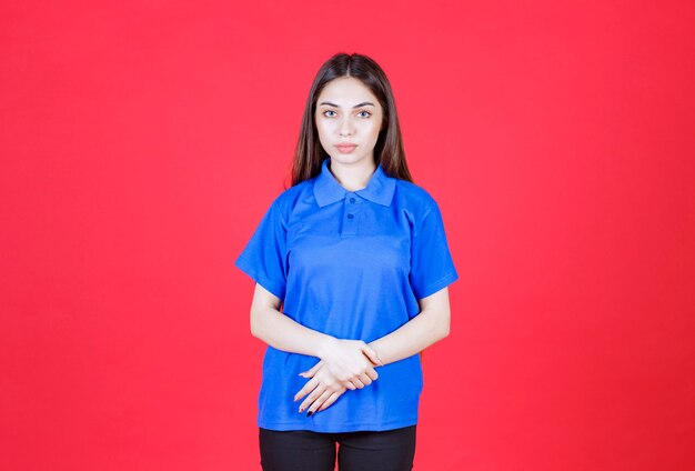 Giovane donna in camicia blu in piedi sul muro rosso