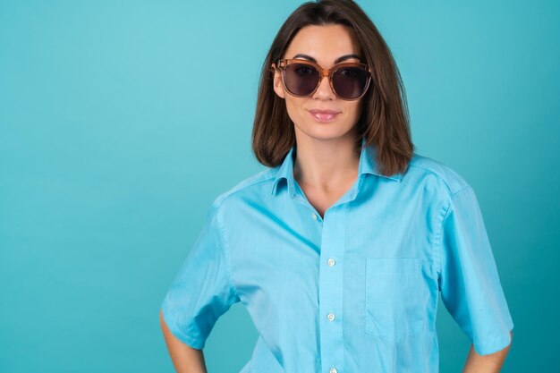 Young woman in a blue shirt on a wall in sunglasses, fashionably stylish posing