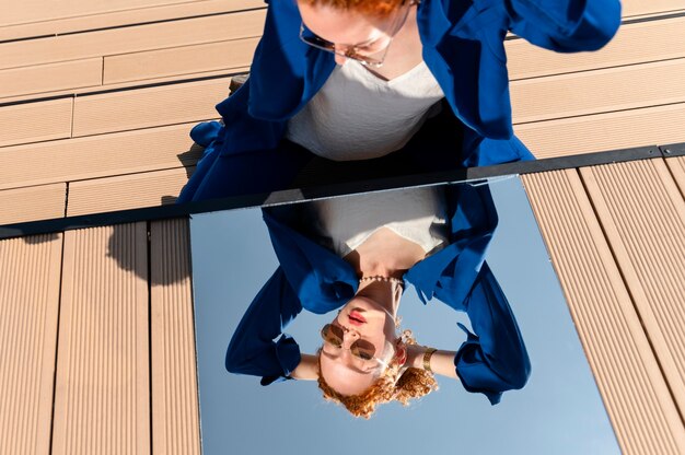 Young woman in blue suit posing with mirror on wooden slats