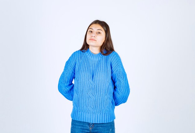 young woman in blue sweater standing on white.