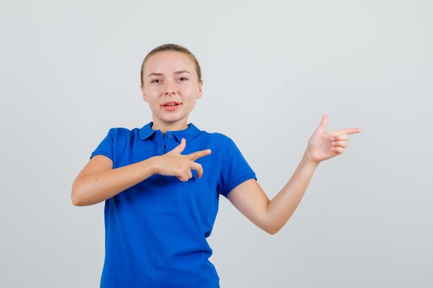 Young woman in blue t-shirt pointing to side and looking cheerful