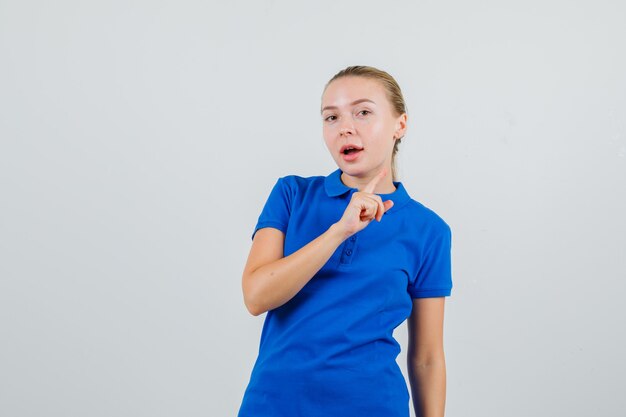 Young woman in blue t-shirt pointing up and looking curious