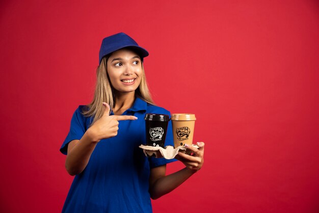 Young woman in blue uniform pointing at a carton of two cups.