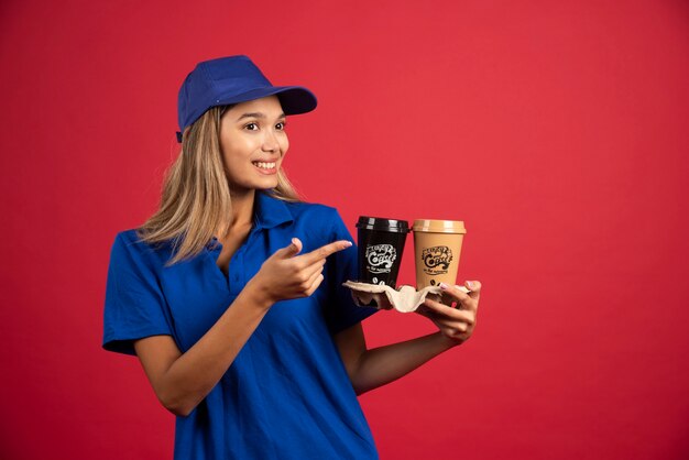 Young woman in blue uniform pointing at a carton of two cups. 