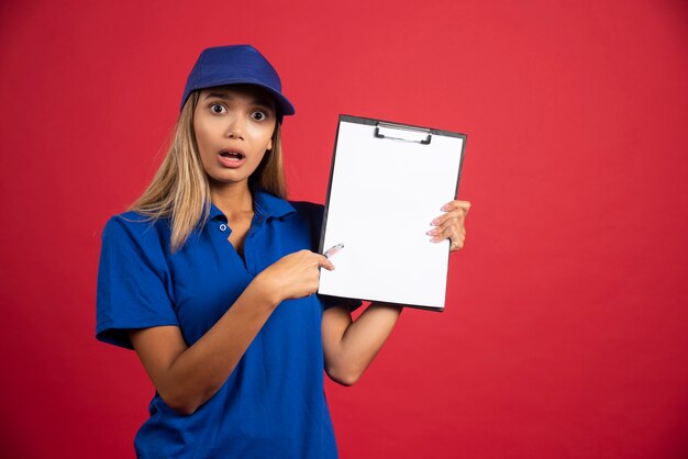 Young woman in blue uniform pointing at clipboard with pencil .