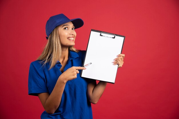 鉛筆でクリップボードを指している青い制服を着た若い女性。