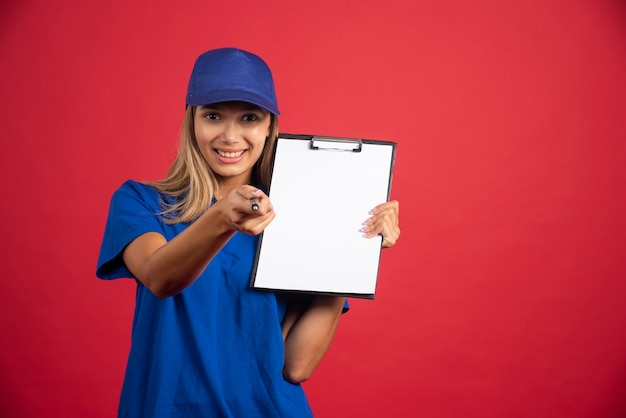 Young woman in blue uniform with clipboard pointing at camera with pencil . 