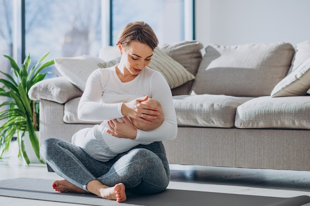 幼児の息子に授乳し、マットの上に座っている若い女性