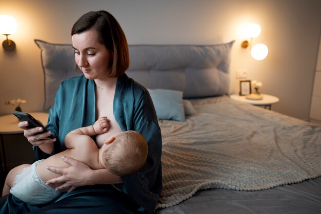 Young woman breastfeeding her cute baby while checking her phone