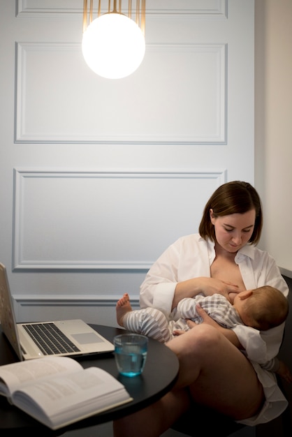 Free photo young woman breastfeeding her cute baby while working
