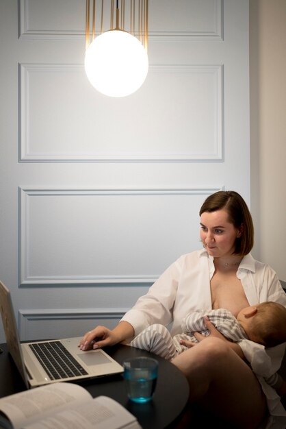 Free photo young woman breastfeeding her cute baby while working