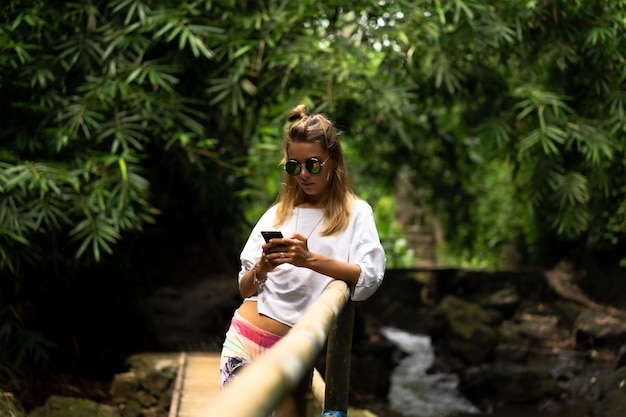 A young woman in bright clothes and sunglasses uses a smartphone