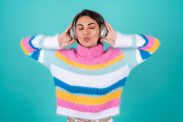 Young woman in a bright multicolored sweater on blue in large noise canceling headphones