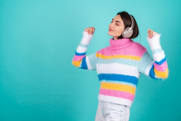 Free photo young woman in a bright multicolored sweater on blue in large noise canceling headphones