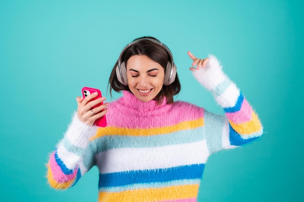 Free photo young woman in a bright multicolored sweater on blue in large noise canceling headphones