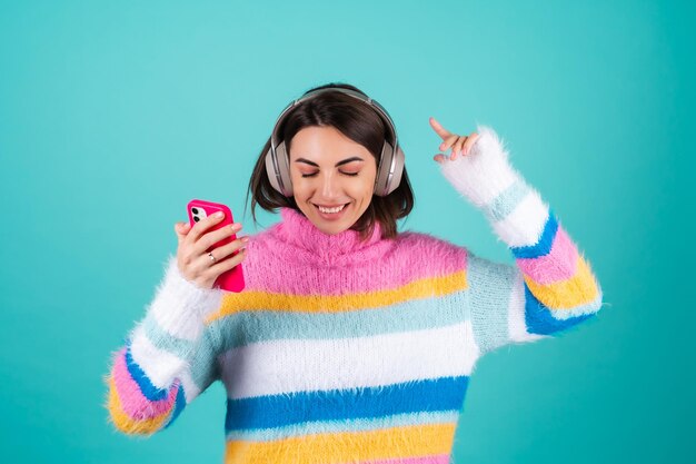 Young woman in a bright multicolored sweater on blue in large noise canceling headphones