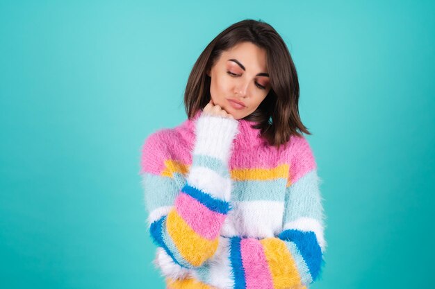 A young woman in a bright multicolored sweater on blue stands with a bored indifferent look