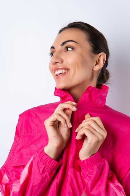 흰색 배경에 밝은 분홍색 스포츠 재킷을 입은 젊은 여성이 세로 프레임으로 밝게 웃고 있습니다.
