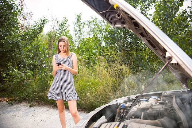 The young woman broke down the car while traveling on the way to rest. She is trying to fix the broken by her own or should hitchhike. Getting nervous. Weekend, troubles on the road, vacation.