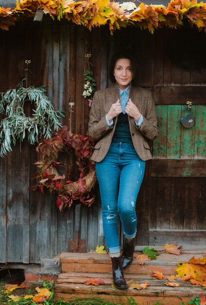 Young woman in a brown warm jacket and jeans poses on a rustic house
