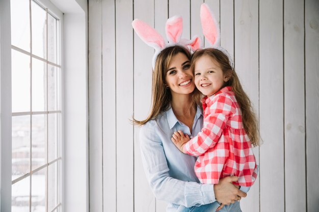 Young woman in bunny ears holding daughter in arms 