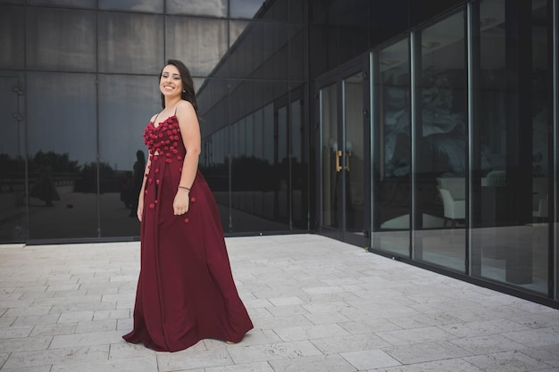 Young woman in a burgundy long evening dress posing on the balcony