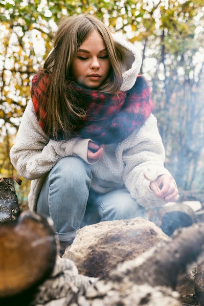 Free photo young woman burning marshmallows in camp fire outdoors