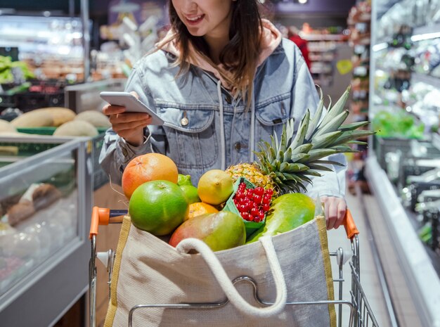 Молодая женщина покупает продукты в супермаркете с телефоном в руках.