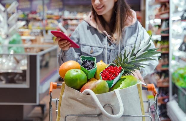 Молодая женщина покупает продукты в супермаркете с телефоном в руках