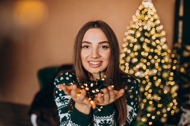 Young woman by the Christmas tree with christmas glowing lights