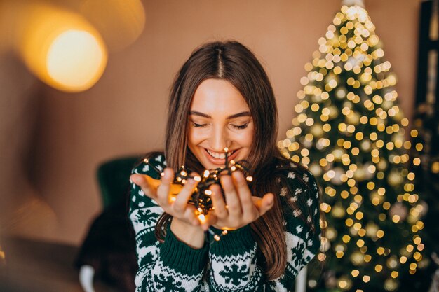 Young woman by the Christmas tree with christmas glowing lights