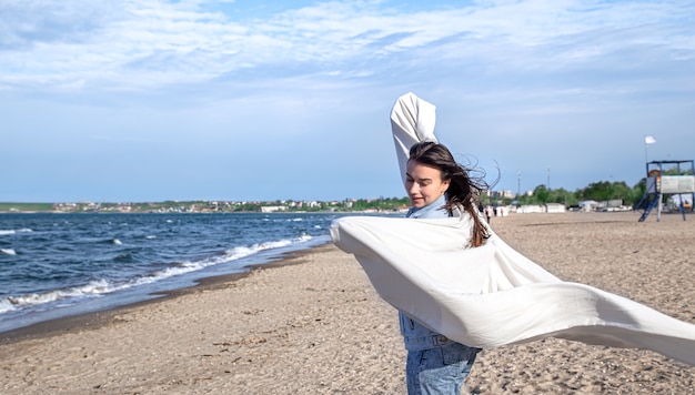 海沿いの若い女性は、大きなシートを風に抱いて楽しむ、自由なライフスタイル。