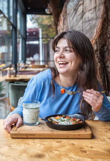 A young woman in a cafe dines on traditional shakshuka and ayran