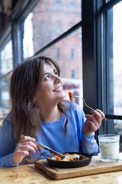 A young woman in a cafe dines on traditional shakshuka and ayran